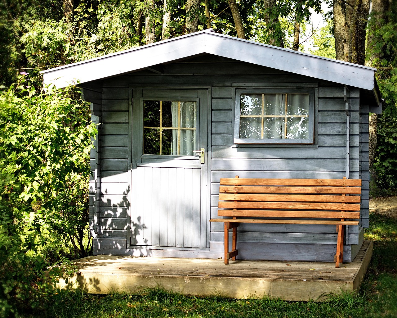 Abri de jardin en bois installé au fond d'un jardin arboré